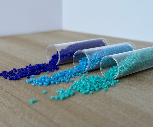 Three tubes of beads spilled onto a sandstone surface. The beads are dark blue, light blue and blue-green.