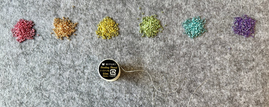 Six piles of beads in varying colours and a spool of thread