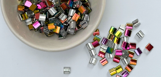 Rainbow tila beads in a bowl and spilled on the desk