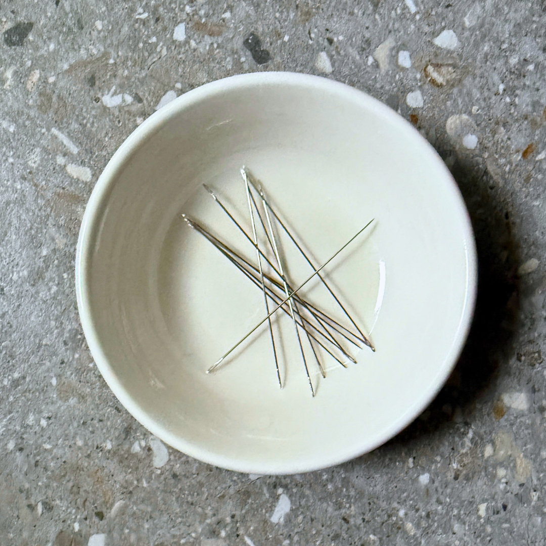 Ten beading needles displayed in a white dish
